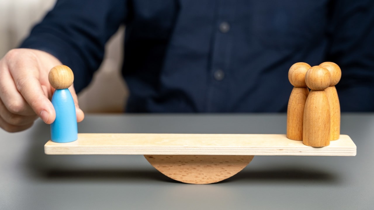 Figura de mano equilibrando una tabla con figuras representando personas, simbolizando el balance en liderazgo.